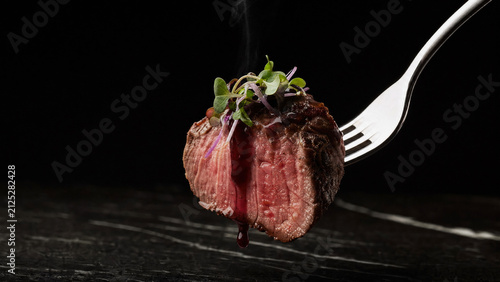 Fork with mediumrare steak bite topped with microgreens