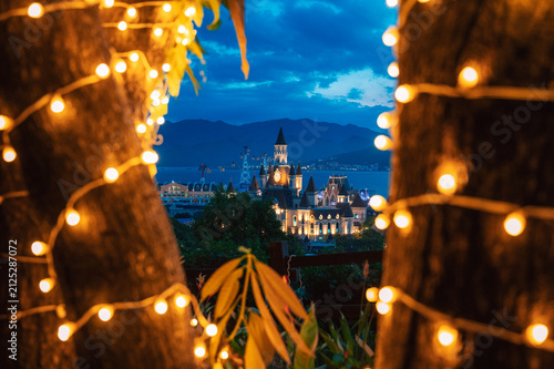 Illuminated castle-inspired of Vinpearl in VinWonders theme park overlook a scenic bay at dusk, creating a magical waterfront cityscape with mountains, dramatic clouds, and evening lights.
