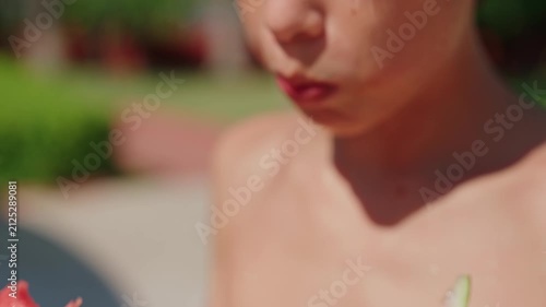 A close-up of a young boy taking a bite of a large, juicy slice of fresh watermelon on a sunny summer day. The vibrant red fruit, visible texture, and refreshing juice highlight healthy seasonal