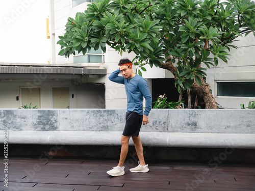 Fit young Asian man in sportswear walking on a wooden deck in an urban setting.