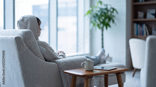 Person relaxing on sofa by window with coffee and tablet