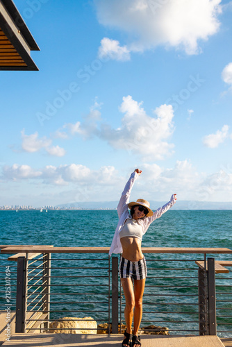The girl enjoys her vacation. A slender woman stands on the embankment near the sea and enjoys the moment. Summer vacation by the sea.