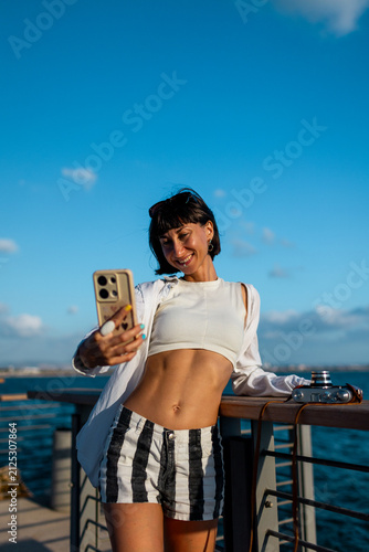 Female blogger shoots content for social networks. Smiling tourist takes a selfie on her mobile phone against the backdrop of the sea.