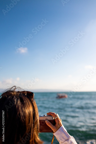 girl taking picture of ship standing on embankment. Beautiful female tourist enjoying sea view while relaxing on weekend. girl using camera.