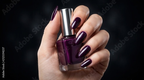 Close up of manicured hands with dark purple nail polish and a bottle.