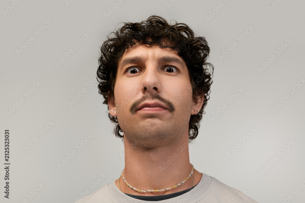 Obraz premium Young man with a distinctive moustache shows a playful expression in a light setting