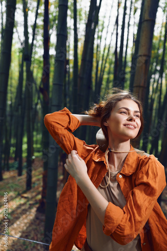 Canvas Print Woman smile bamboo forest portrait outdoor, young female in orange jacket enjoying sunlight in bamboo grove, relaxed expression, natural beauty and travel lifestyle scene