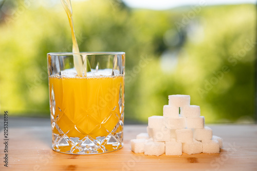 Foto Orange juice is poured into a glass along with a stack of sugar cubes, refreshing beverage