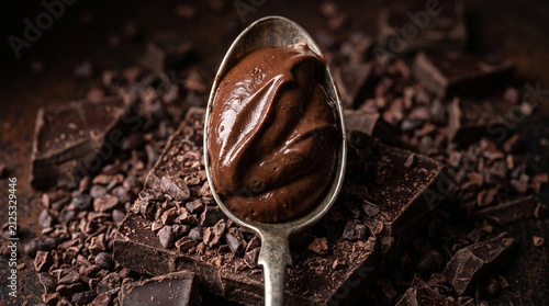 A closeup of a vintage silver spoon filled with rich, creamy chocolate ganache or mousse, resting on a bed of dark chocolate chunks and nibs