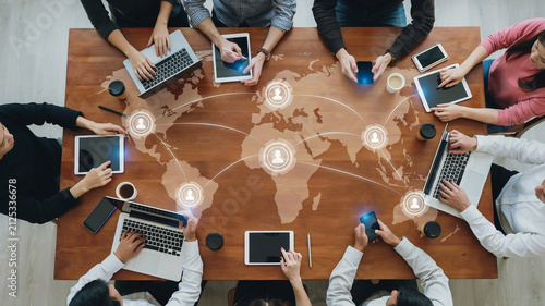 Overhead view of people around a table with a world map and connection nodes group meeting