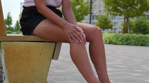 Woman Sitting on Bench and Rubbing Knee in City Park