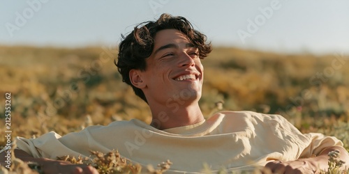 Smiling young man reclining in a grassy meadow at sunset background for lifestyle wallpaper and summer wellness design