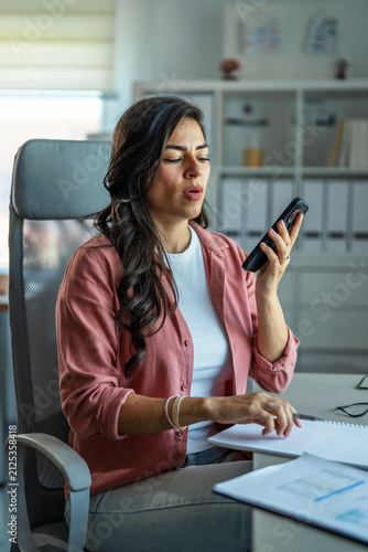 фотографія Woman sending voice message using smartphone in office