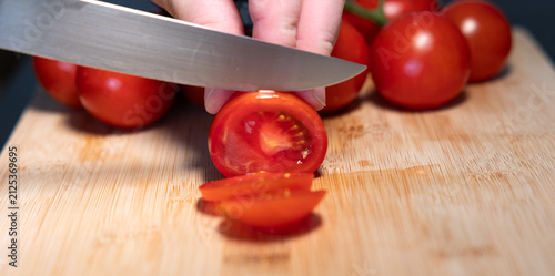 Foto A hand is holding a red tomato on a cutting board and slicing it with a kitchen knife
