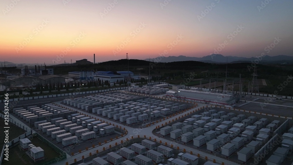 Fototapeta premium Large-scale energy storage power station at sunset with orderly battery arrays and mountain backdrop
