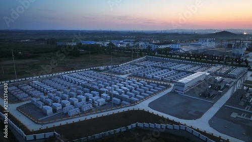 Large-scale energy storage station captured at dusk with aerial view showing modular battery arrays and industrial facility layout