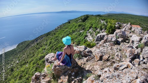 Woman on cliff enjoying panoramic view of sparkling Adriatic Sea and the Sveti Ivan Beach below. Exploring beautiful nature of Cres Island in Croatia. starting point to Sveti Ivan or Lubenice Beach