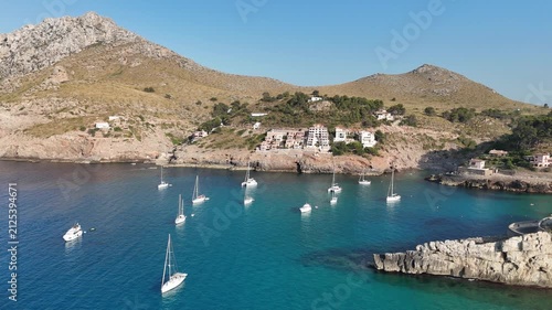 Aerial backward pull-back shot over turquoise bay and anchored boats in Cala Sant Vicenc, Mallorca