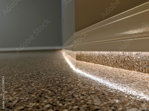 A corner of a residential space features an epoxy-coated garage floor complemented by a baseboard and illuminated by raking light