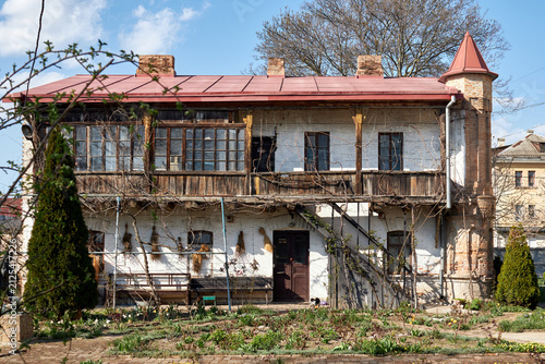 Old rustic house with wooden balcony and garden under blue sky