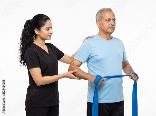 premium indian physiotherapist assisting senior man with resistance band shoulder external rotation exercise isolated on white background for rehabilitation healthcare
