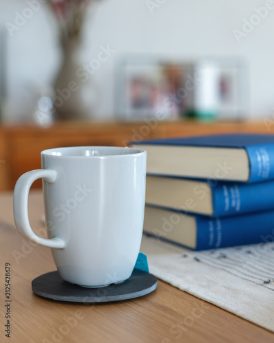 White tea cup beside stack of blue books at home