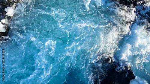 Aerial view of the turquoise waters and white foam of Bruarfoss waterfall surrounded by snow-covered rocks in Blaskogabyggd, Blaskogabyggd, Iceland.