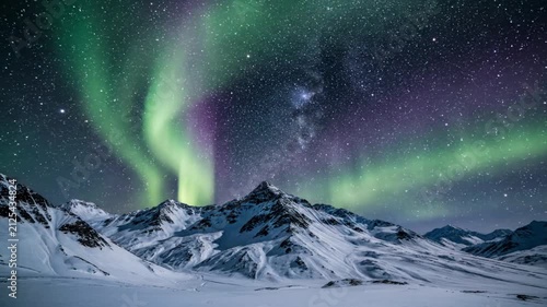 Aurora borealis and Milky Way over snow-covered mountain peaks at night.