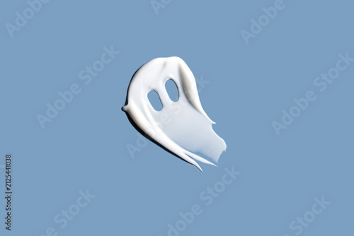 Cream smear in the shape of a cute ghost isolated on blue background. Spooky ghost on pastel blue background. Halloween beauty concept.
