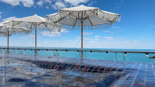White woven beach umbrellas overlooking the turquoise sea and blue sky at a luxury resort pool deck