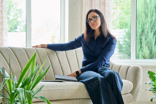Thoughtful businesswoman leaning on sofa looking at camera during work break at home office