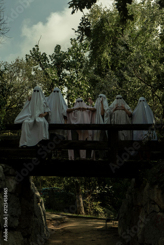 People Dressed as Ghosts Standing on a Wooden Bridge in a Forest