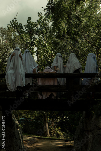 People Dressed as Ghosts Standing on a Wooden Bridge in a Forest