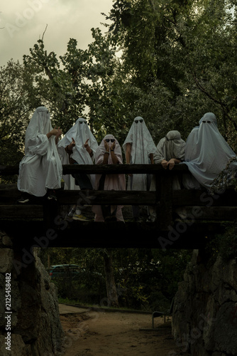 People Dressed as Ghosts Standing on a Wooden Bridge in a Forest