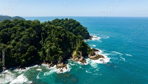 Aerial view of a tropical green forest on a rocky headland meeting the blue ocean.