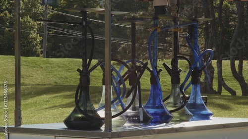 A row of glass hookahs stand on the counter of a street bar in the park