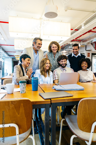 Diverse business professionals smiling, actively working together at a long table in a modern coworking office environment, fostering teamwork and partnership