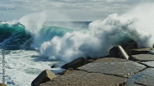 Dramatic ocean wave crashing against rocky breakwater creating a stunning display of power and nature's beauty