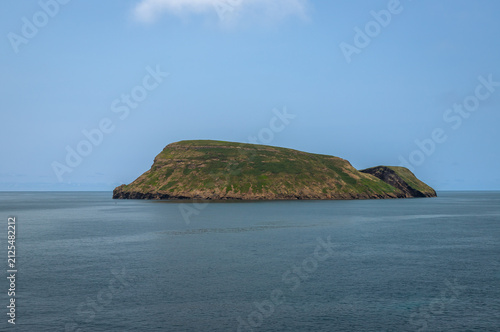 View of Ilhéu de Cabras from Cruz do Canário viewpoint on Terceira Island, Azores, Portugal, featuring two volcanic islets rising from the Atlantic Ocean under a calm blue sky