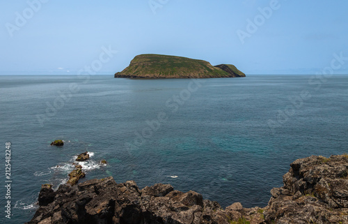 View of Ilhéu de Cabras from Cruz do Canário viewpoint on Terceira Island, Azores, Portugal, featuring two volcanic islets rising from the Atlantic Ocean under a calm blue sky