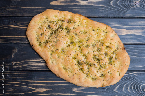A gluten free focaccia sits on a wooden table in the afternoon light.