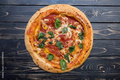 gluten-free Pizza sits on a dark wooden table. It has cheese and tomato sauce.