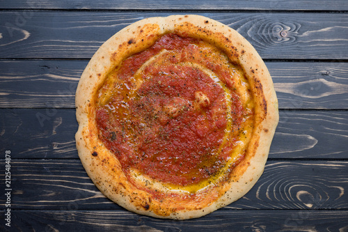 A round gluten free pizza rests on a dark wooden table.