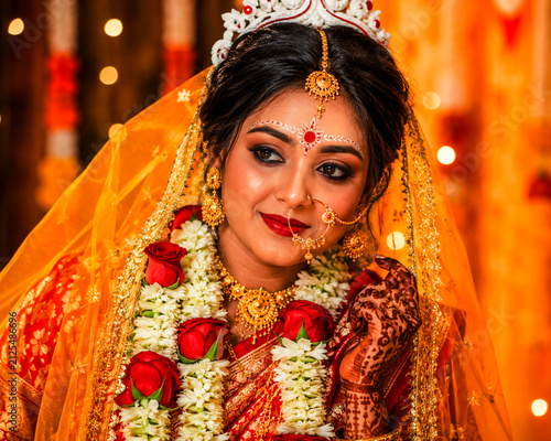 Radiant Bride: A stunning bride adorned in traditional wedding attire, complete with elaborate jewelry, a veil, and henna art, gazes coyly with a gentle smile on her special day.