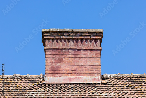 An old Tuscan-style brick chimney situated on a tiled roof under a clear sky. A brick chimney featuring traditional decorative masonry techniques