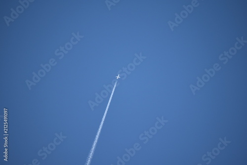 Bild auf Leinwand An aircraft leaving a condensation trail, or contrail, in a clear sky
