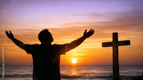A silhouette of a man in a prayerful pose against the backdrop of a beautiful sunset over the ocean. He stands near a wooden cross, symbolizing faith and spirituality.