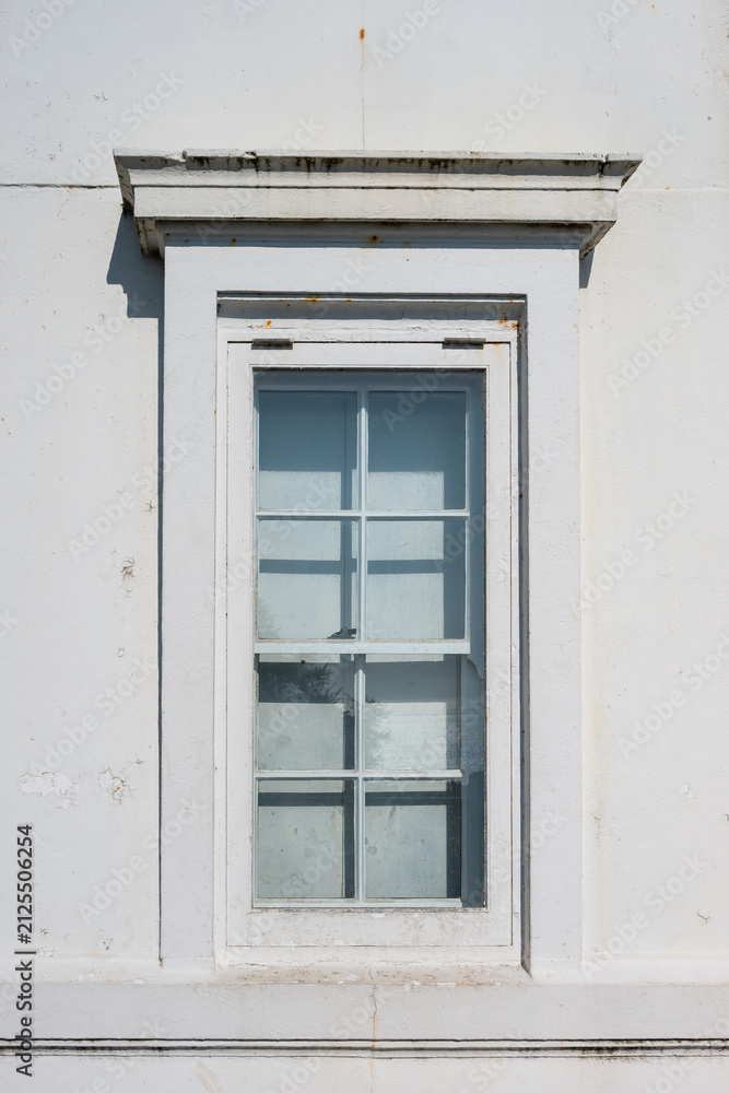 Fototapeta premium Old architectural window in classic colonial style with wood frame, exterior white wall, single-hung sash with grids 