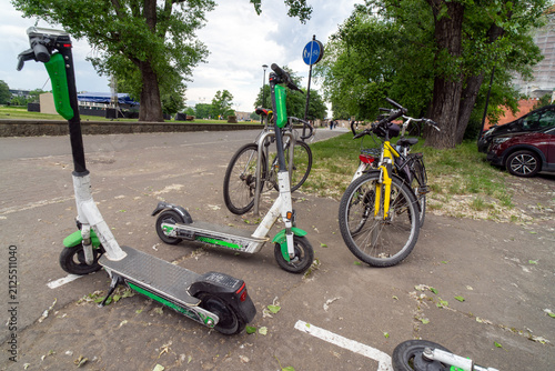 Several bicycles and electric scooters parked together. These modes of transportation are used for active travel on campuses and in cities. E-scooters, rental option in cities. To rent and park. 
