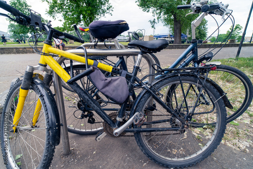 Parked bicycles secured to a metallic hoop stand, used for short-term urban parking.  Appear to be a mix of styles, including a yellow mountain bike and another with a rear pannier rack and cargo bag.